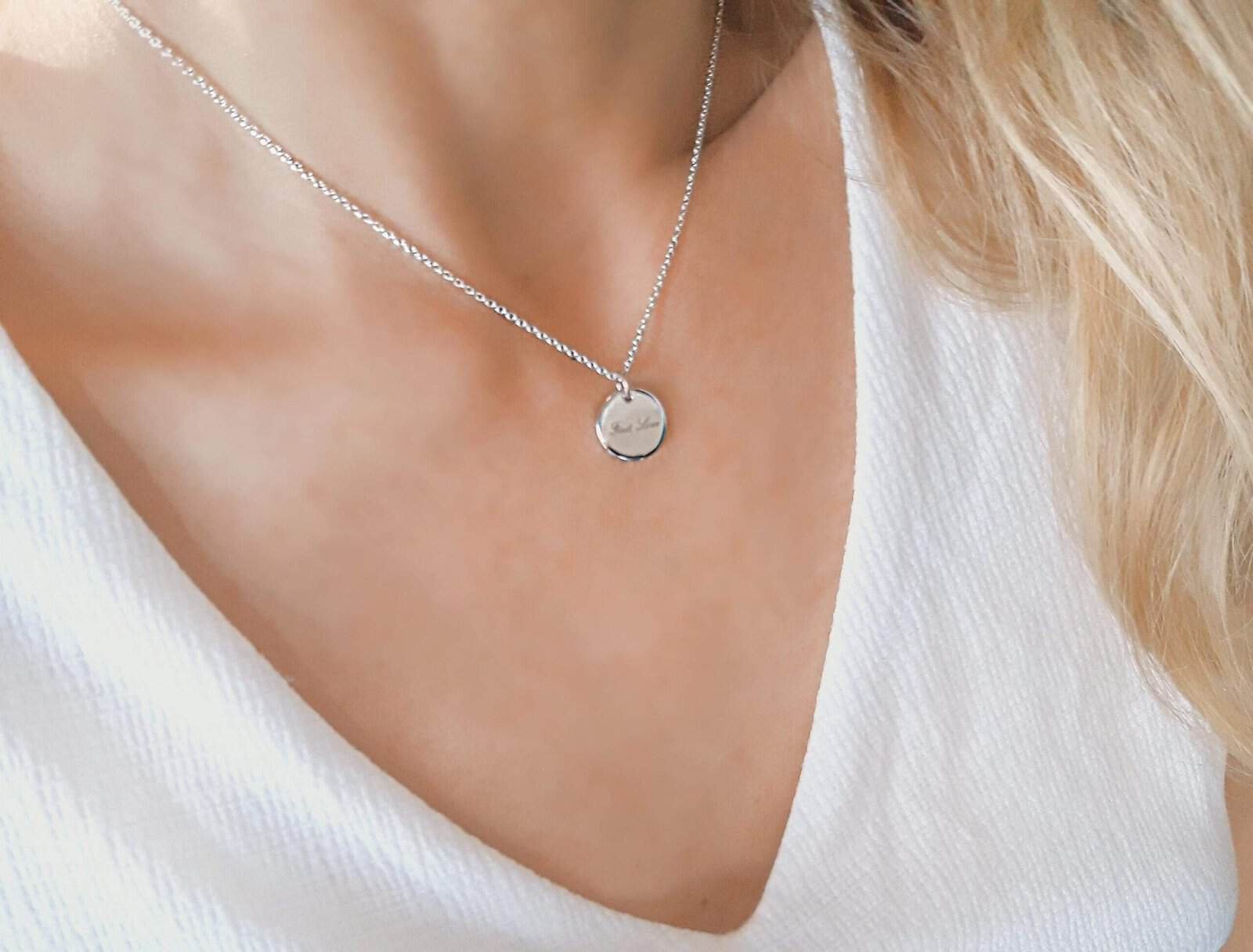 Élégant collier en argent sterling avec pendentif rond gravé, porté sur un décolleté en V avec une tenue blanche raffinée. Parfait pour un style chic et sophistiqué en bijoux fantaisie.