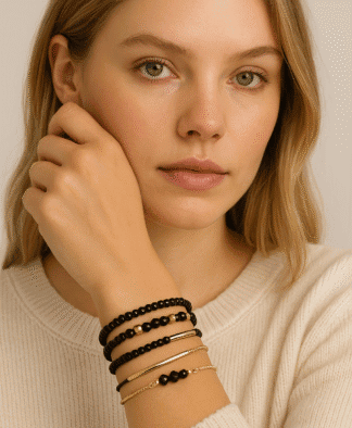 Bracelets en perles noires et fines chaînes dorées, élégants et tendance, portés par une jeune femme à la peau claire et aux cheveux blonds, parfaits pour un look sophistiqué ou casual.