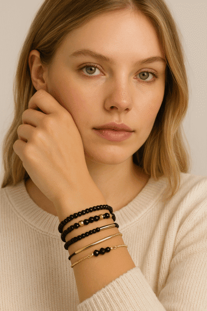 Bracelets en perles noires et fines chaînes dorées, élégants et tendance, portés par une jeune femme à la peau claire et aux cheveux blonds, parfaits pour un look sophistiqué ou casual.