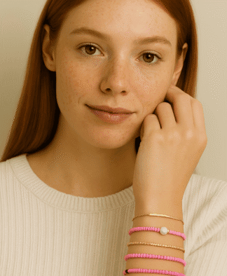 Bracelets en perles roses, or doré et perle blanche, accompagnant un pull crème, montés sur un poignet délicat d'une femme aux cheveux roux, idéal pour la mode féminine tendance.