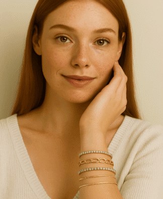Légère photo d'une jeune femme aux cheveux roux, portant plusieurs bracelets dorés ornés de pierres brillantes, avec un maquillage naturel et un sourire subtil, mettant en valeur ses accessoires de mode élégants.
