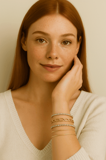 Légère photo d'une jeune femme aux cheveux roux, portant plusieurs bracelets dorés ornés de pierres brillantes, avec un maquillage naturel et un sourire subtil, mettant en valeur ses accessoires de mode élégants.