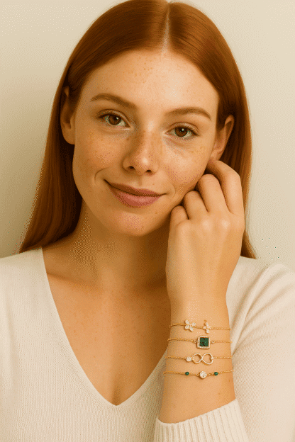 Bracelets en or avec pendentifs variés, ornés de pierres précieuses et de motifs floraux, portés au poignet d'une femme aux cheveux roux et à la peau claire, élégante et sophistiquée.